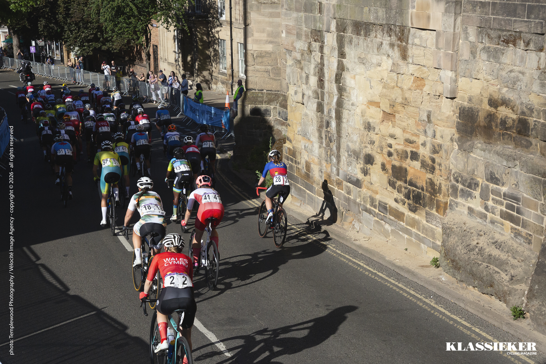 Birmingham 2022 - Women pass in front of the stone side of the remains of Warwick’s walls during the road race