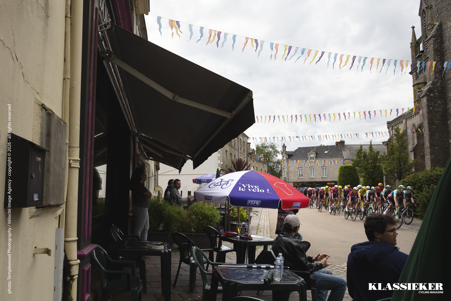 Spectators watch from the outside seating of a nearby cafe as riders race through the village square in Plumelec