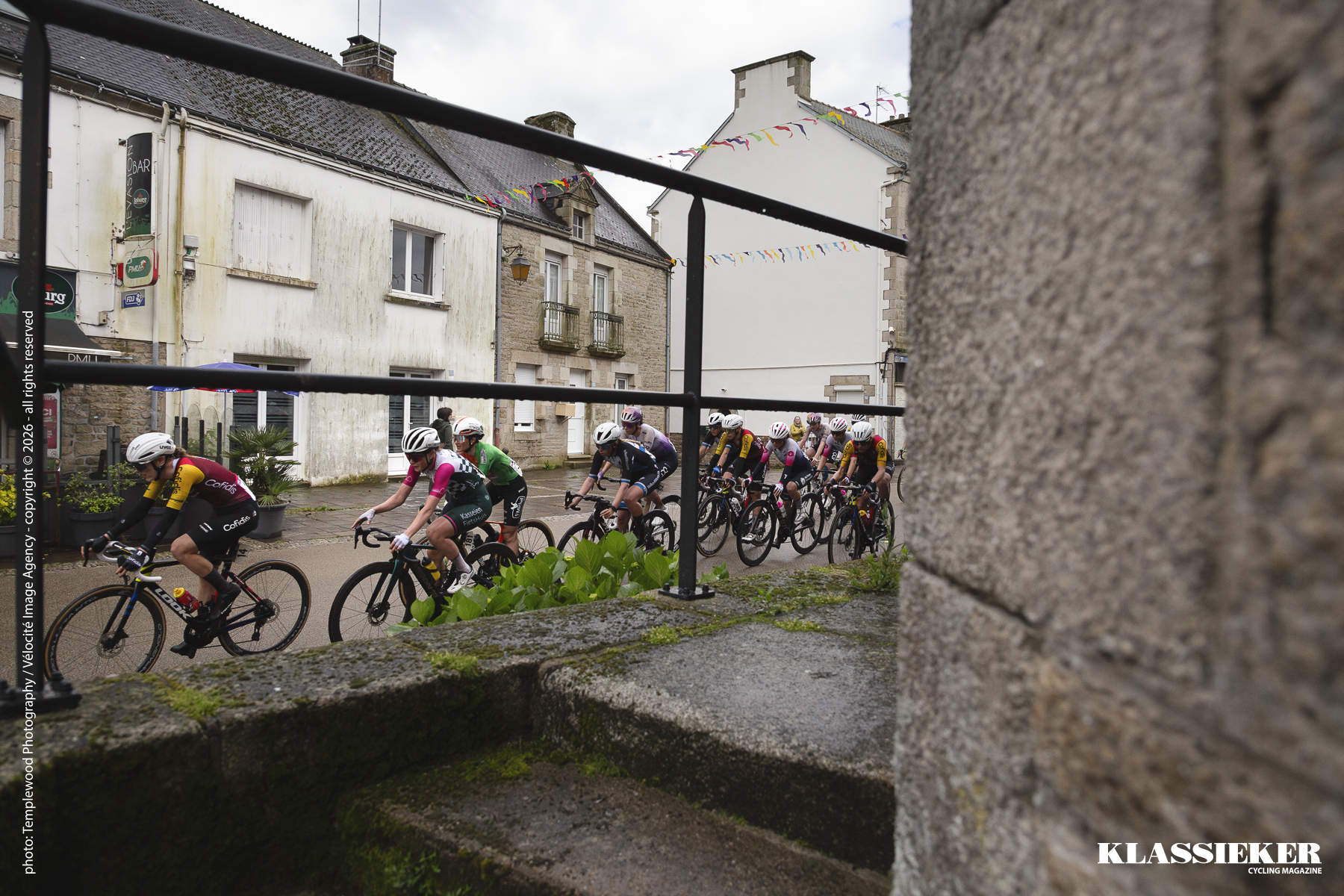 The peloton in the main square in Plumelec. The church steps in the foreground, a row of traditional French houses in the background