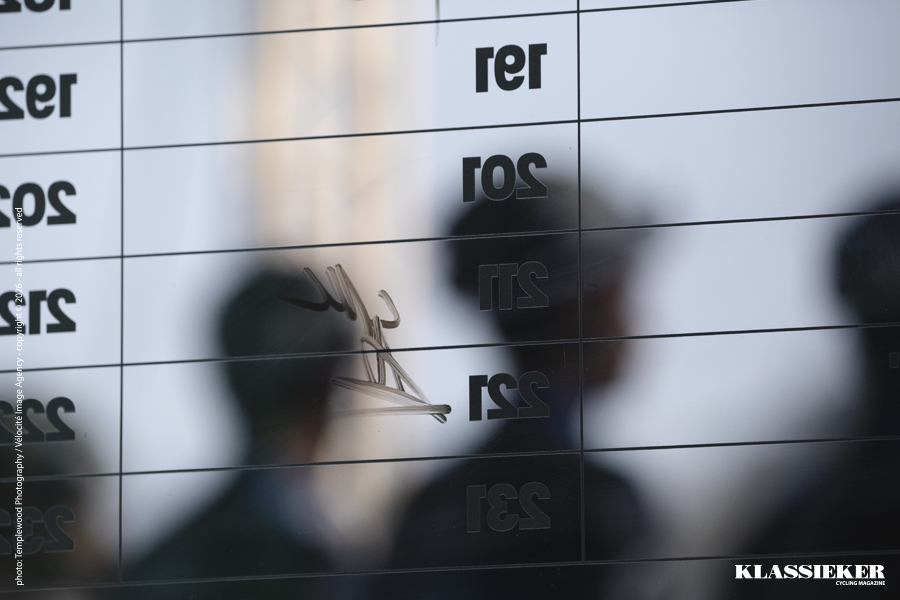 Riders seen through a clear sign-on board as they sign on to the race and are presented to crowd