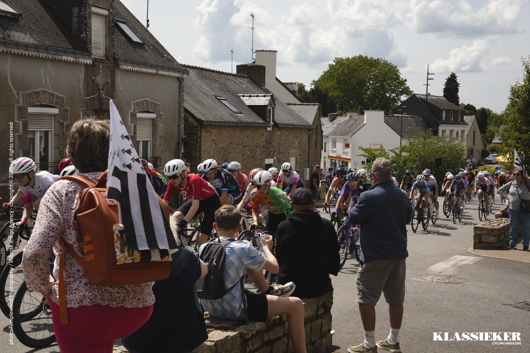 A small crowd watches the race as it passes through the village of Pluvigner. Some have Bretton flags sticking out of their bags