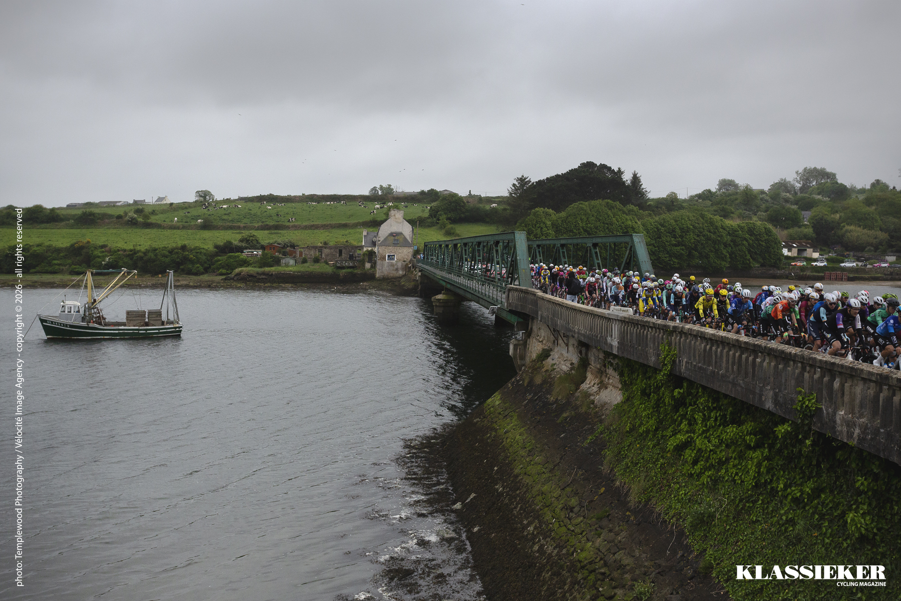 Tro Bro Leon 2026 - Riders cross a bridge over an inlet with a fishing boat in the water